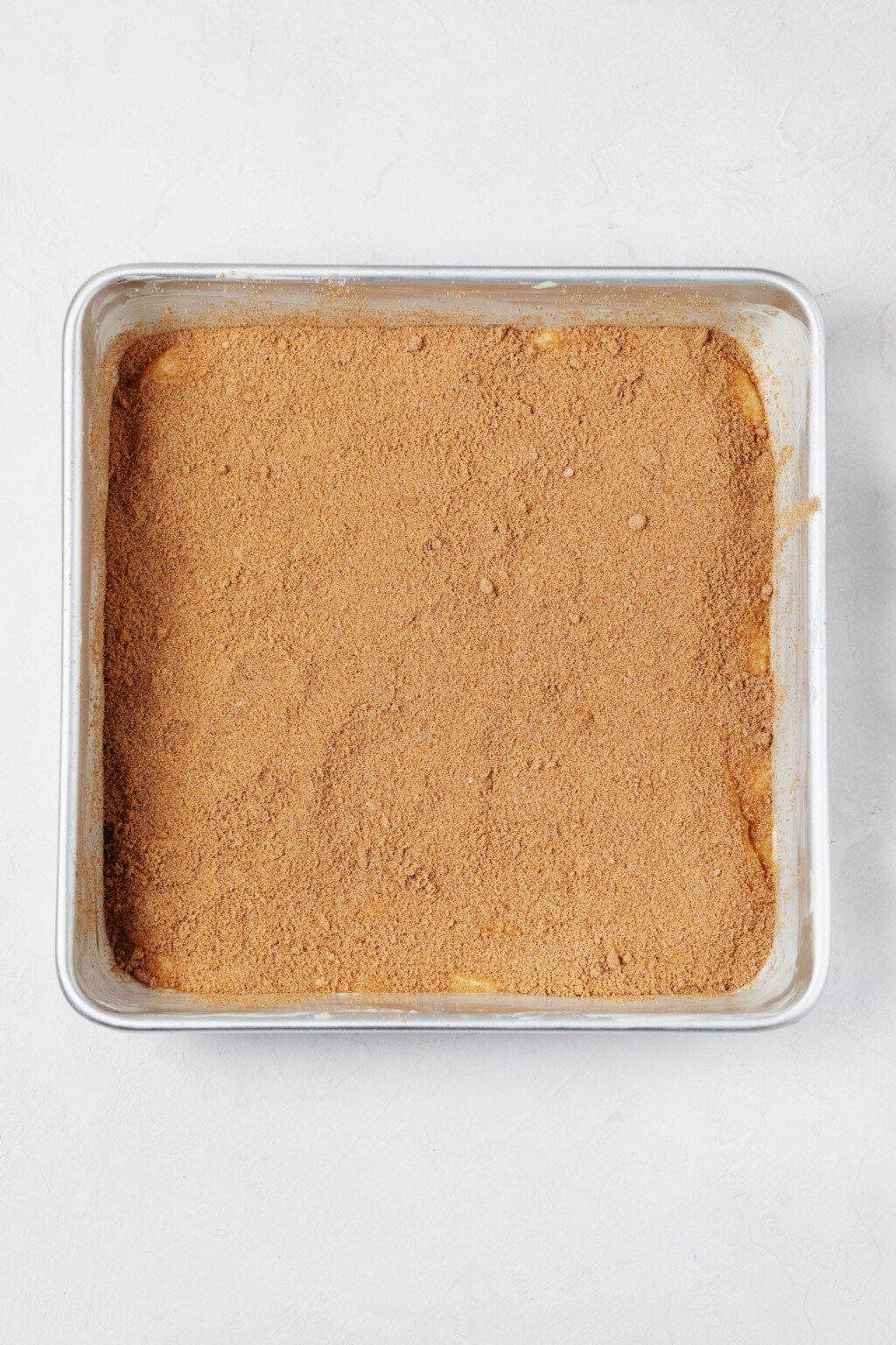A square cake pan is pictured. It holds cake batter topped with cinnamon sugar.