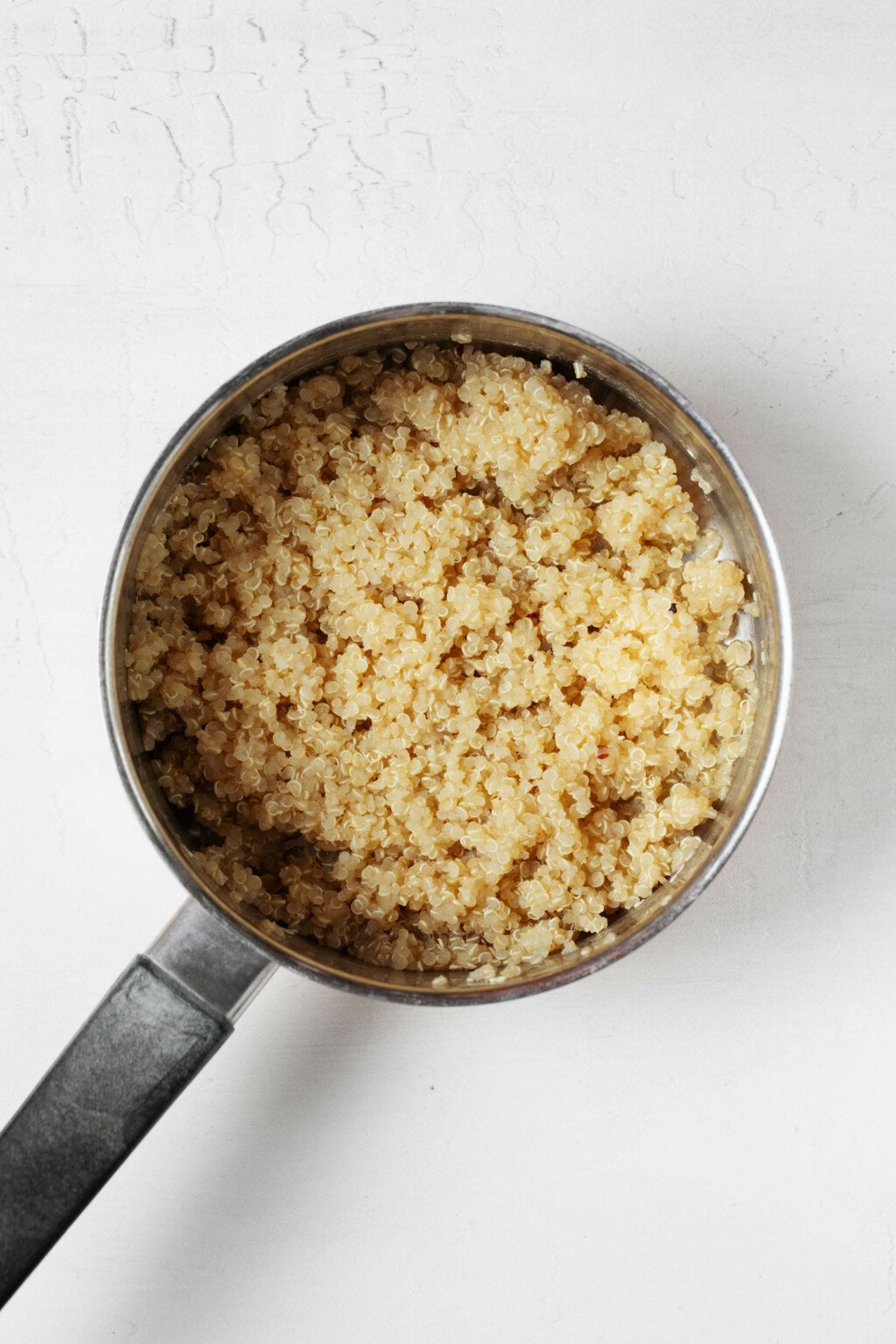 An overhead image of a silver saucepan, which is filled with fluffy, cooked quinoa.