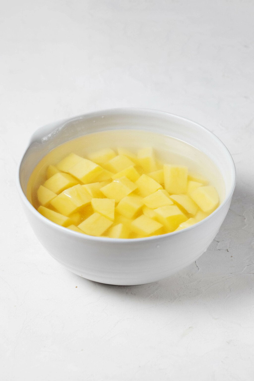 A large white mixing bowl is filled with water. It's being used to soak cubed potatoes.