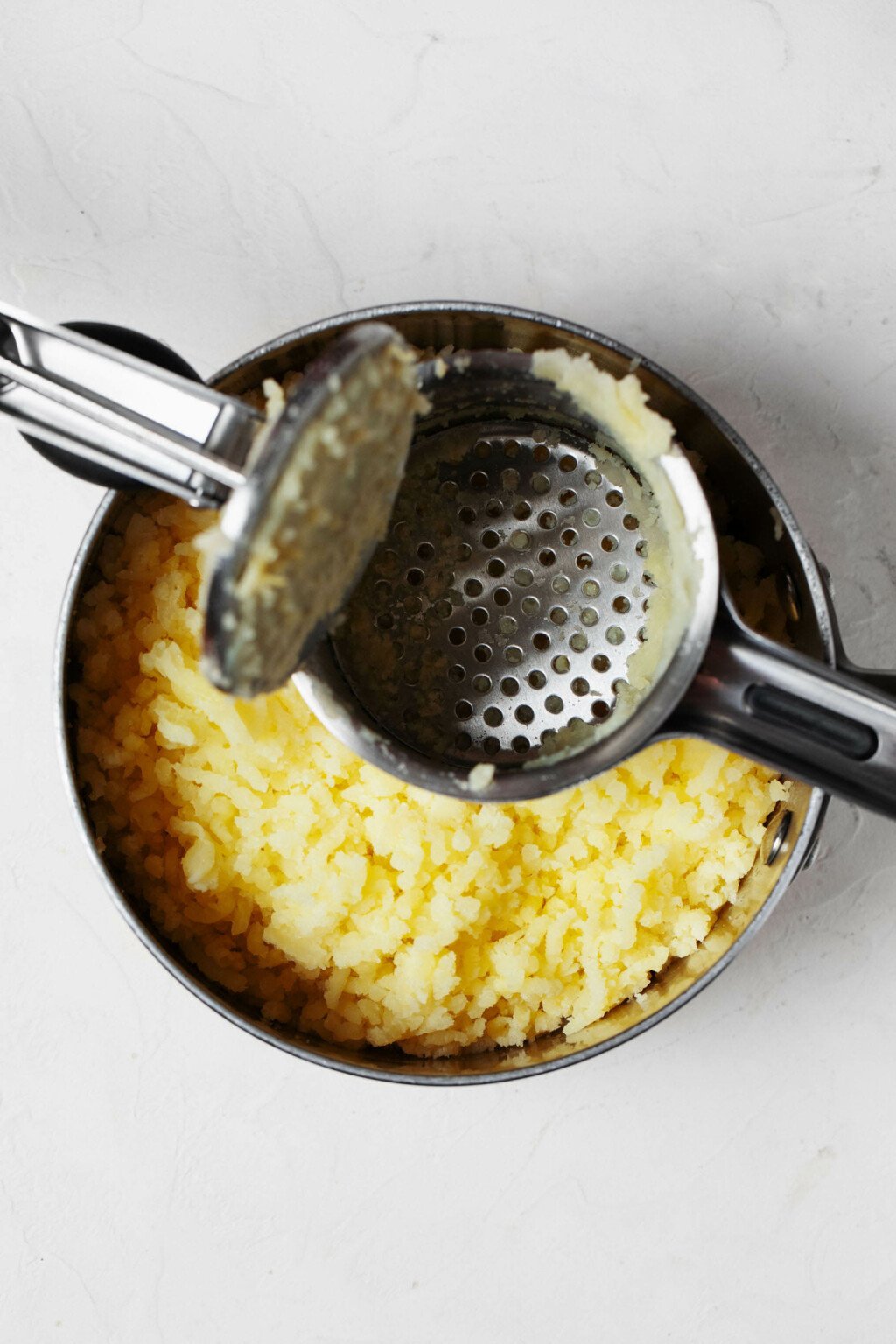 An overhead image of a potato ricer, which is being used to rice pale gold potatoes.
