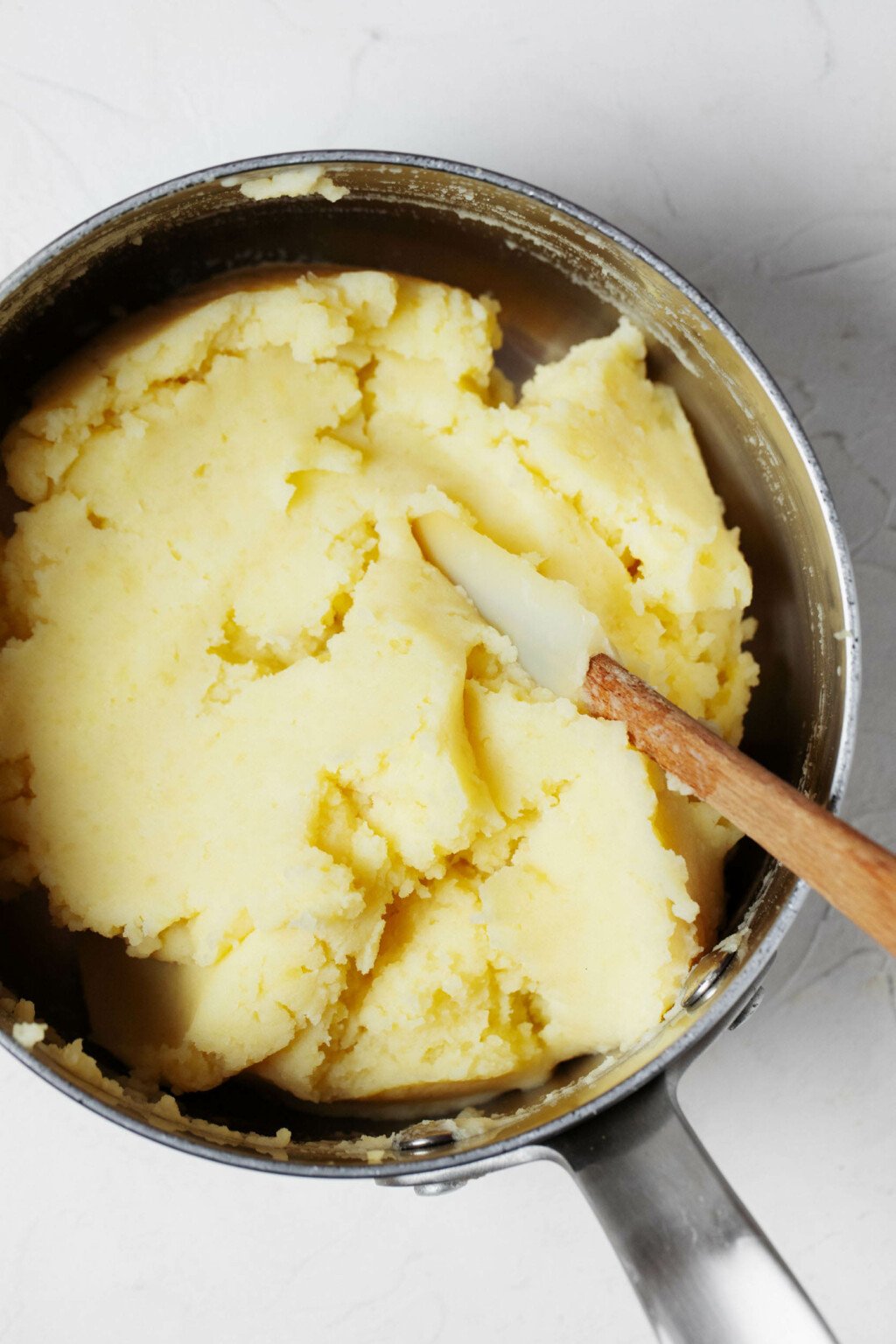 A silver pot is pictured from above. It contains mashed potatoes that are being mixed with a spatula.