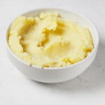 A round white bowl is filled with fluffy, smooth, and creamy vegan mashed potatoes.