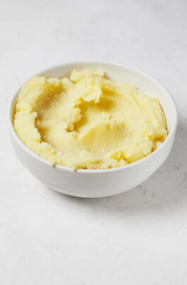 A round white bowl is filled with fluffy, smooth, and creamy vegan mashed potatoes.
