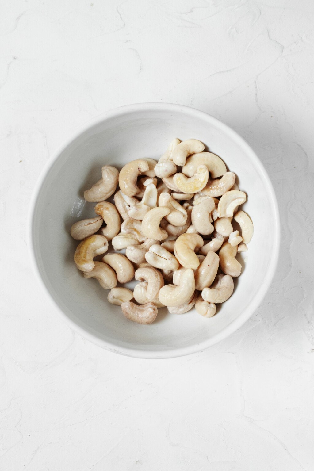 An overhead image of a small bowl of soaked cashews.