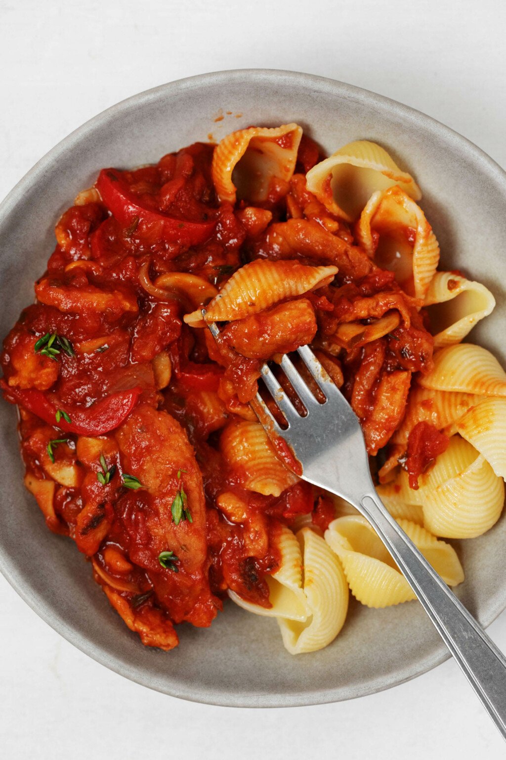 A bowl of shell pasta has been topped with red sauce and a vegan protein.