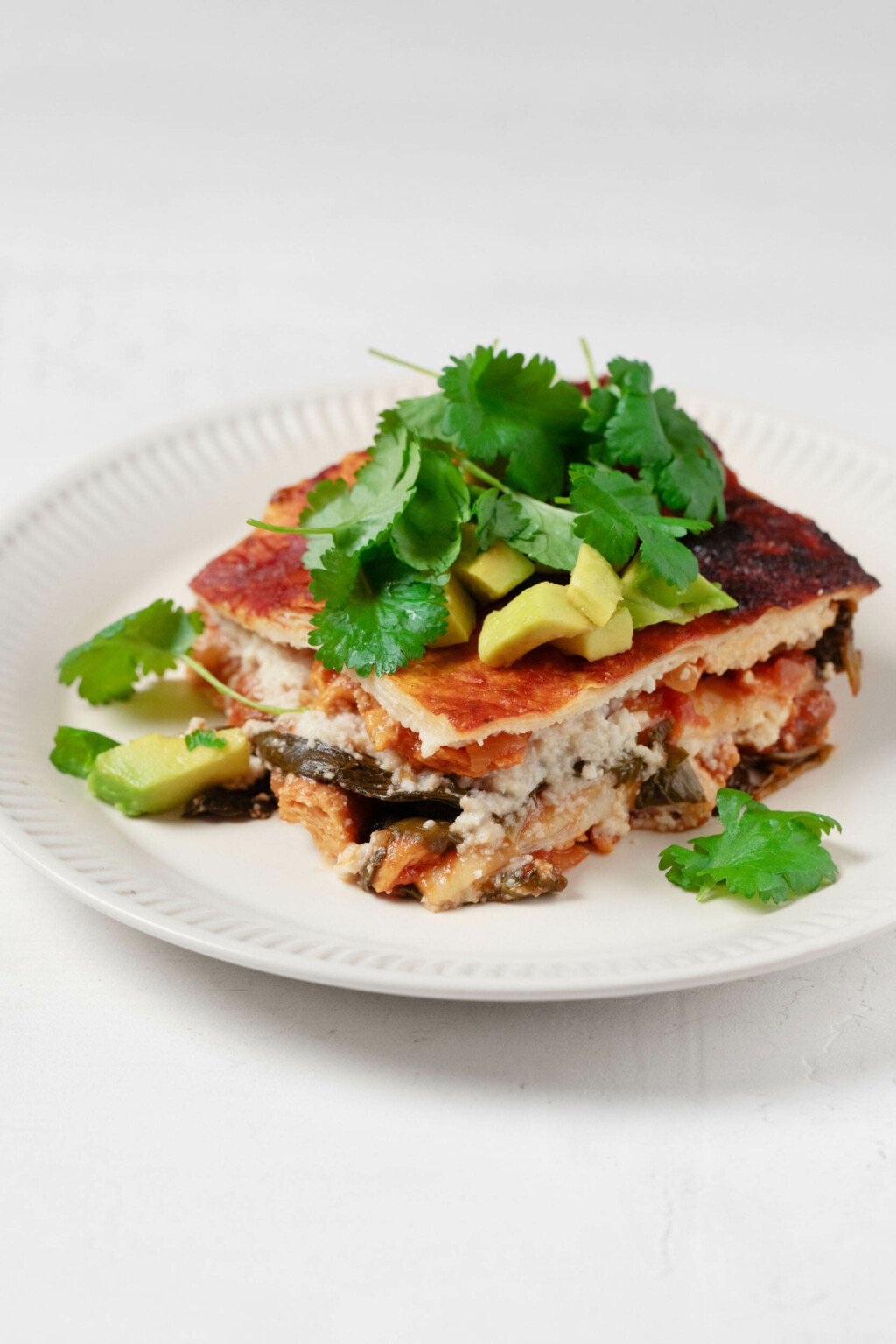 An angled image of vegan enchilada casserole, resting on a white plate.