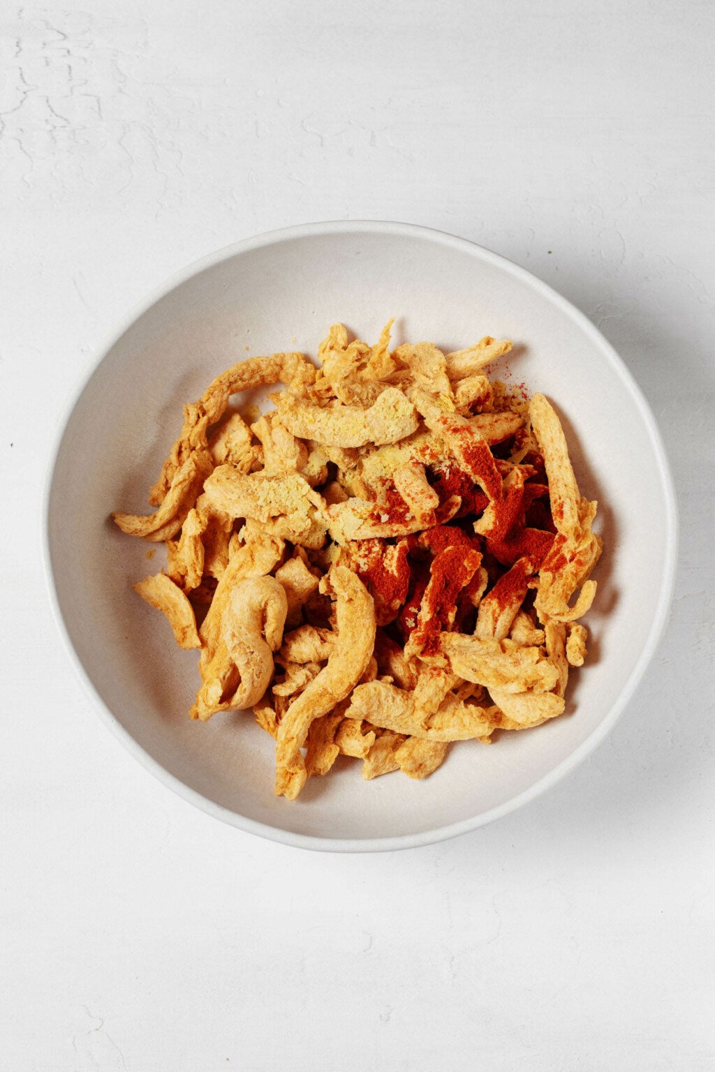 A large, white mixing bowl is being used to hold dry vegan soy curls.