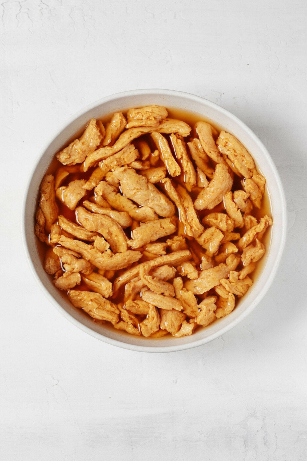 An overhead image of a white mixing bowl, filled with hot broth and a plant-based protein.