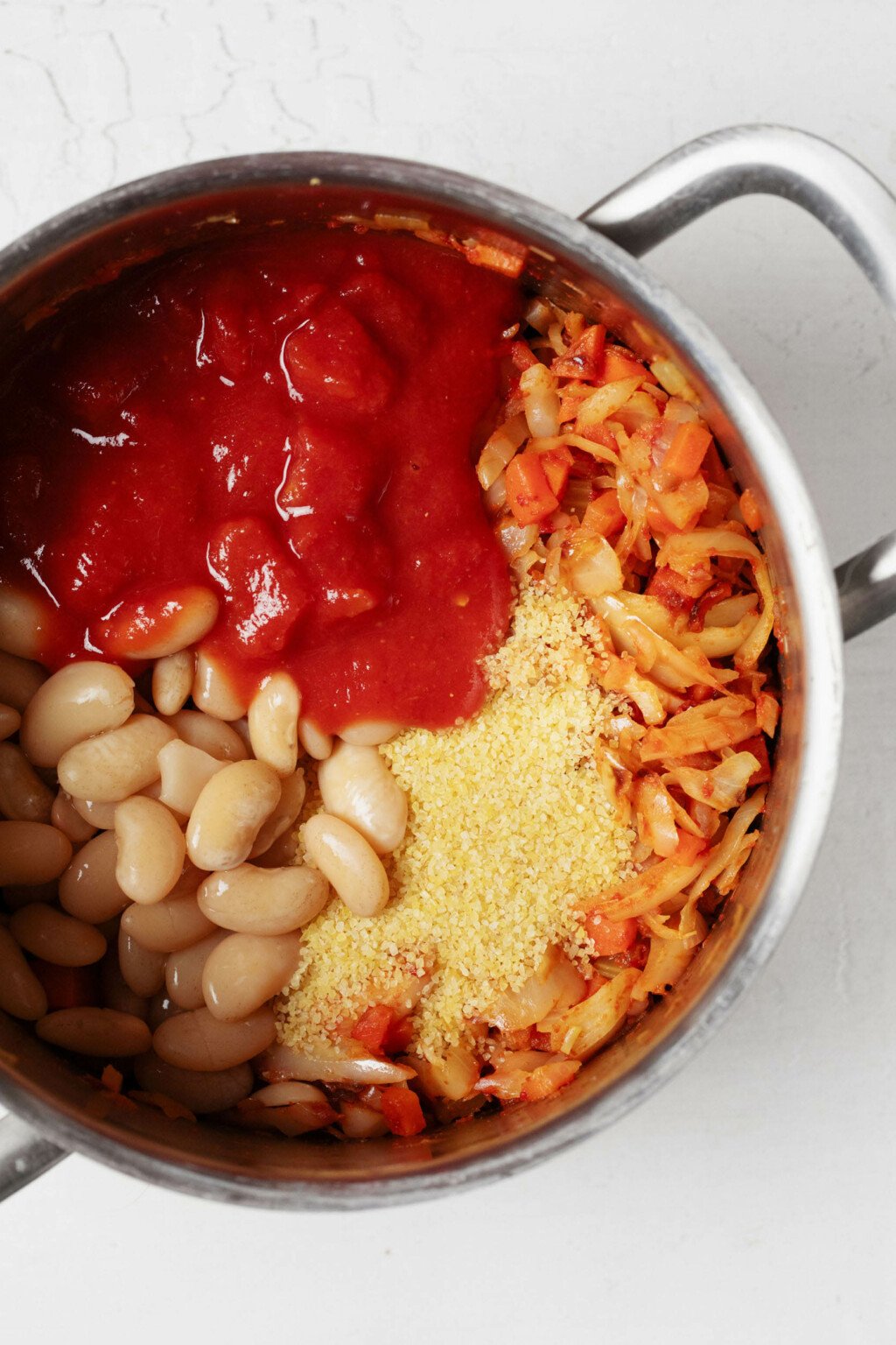 An overhead image of a silver pot, filled with navy beans, cabbage, bulgur wheat, and tomatoes.