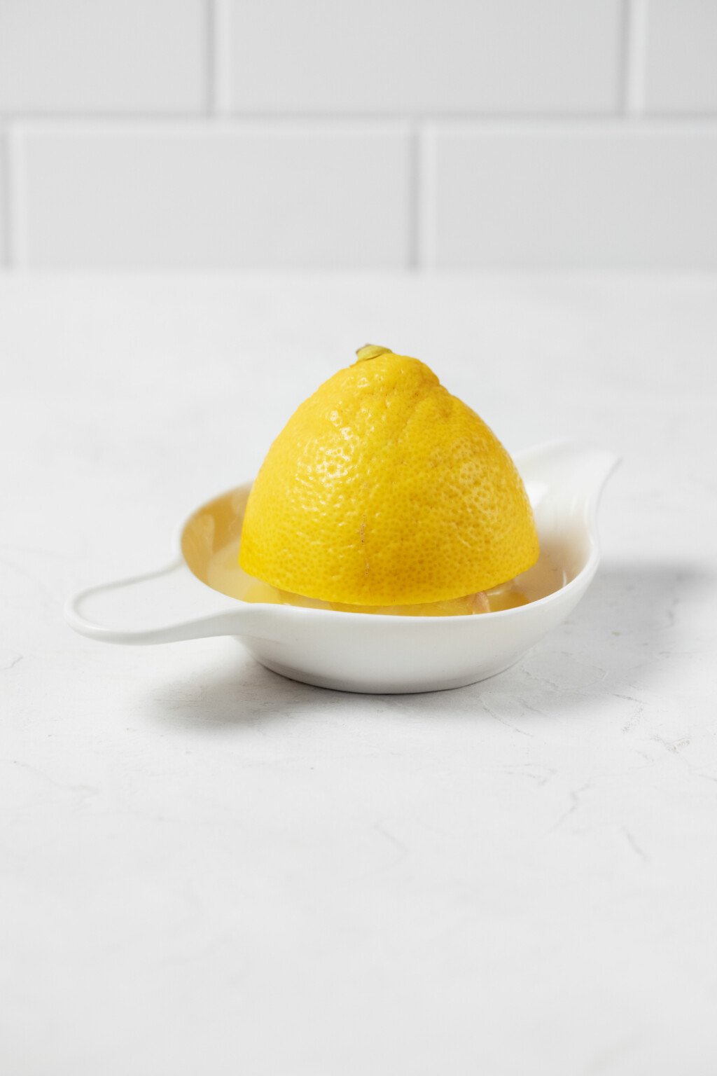 An image of a half lemon in a lemon squeezer, resting on a white surface.
