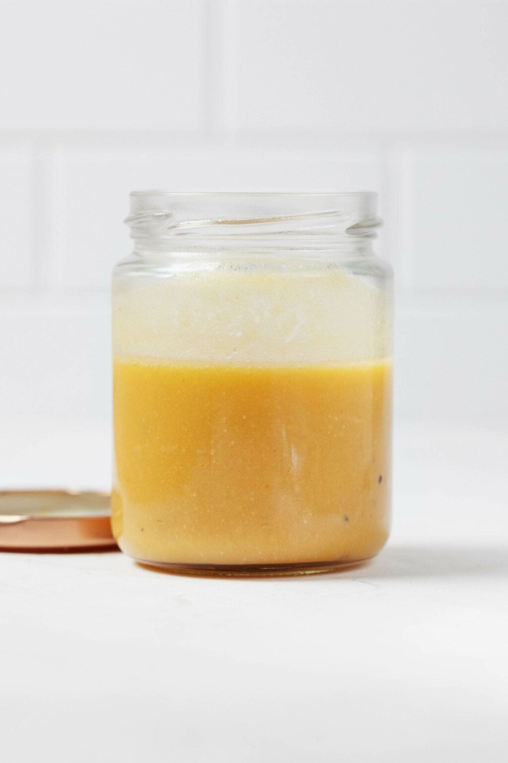 An angled image of a clear, small mason jar, which is filled with a creamy miso vinaigrette. The vinaigrette contains orange juice and has a pale orange color.