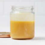 An angled image of a clear, small mason jar, which is filled with a creamy miso vinaigrette. The vinaigrette contains orange juice and has a pale orange color.