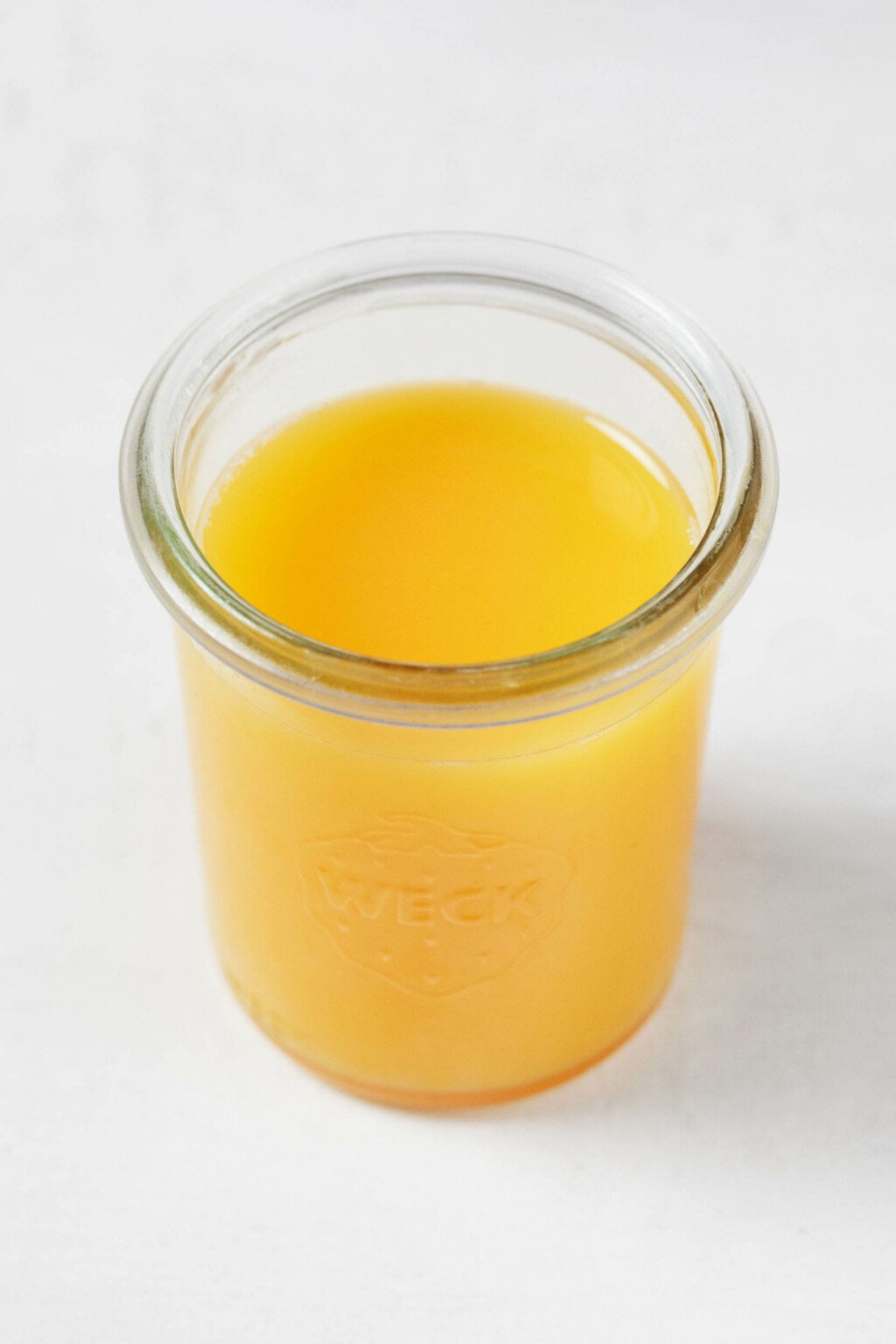 An image of a clear Weck mason jar, which is being used to hold bright golden orange juice.