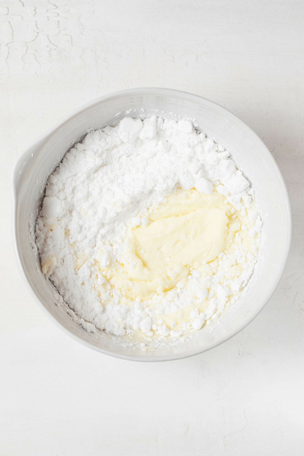 An overhead image of a white bowl, filled with powdered sugar and a creamy base of butter.