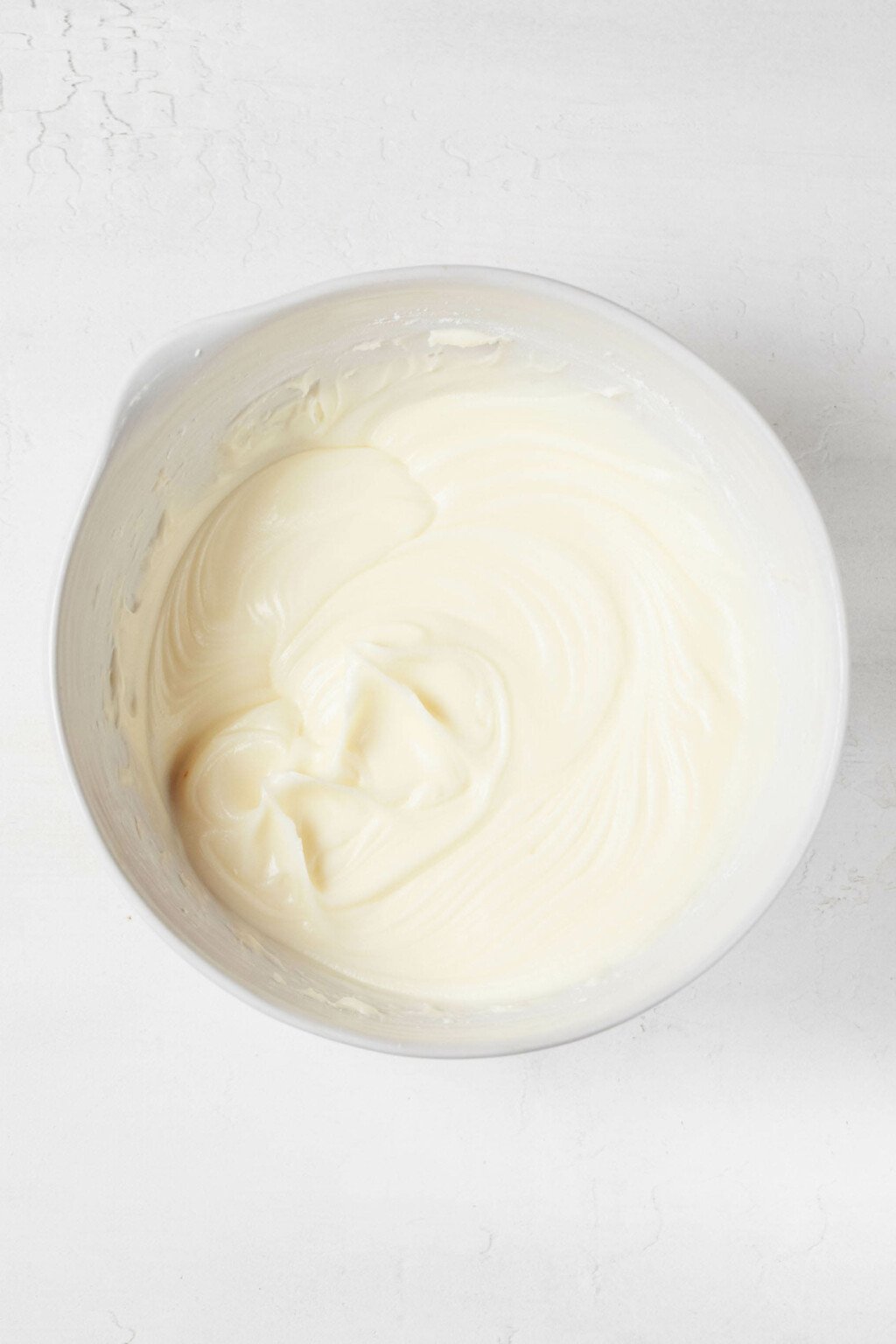 An image of a white bowl, which is filled with freshly beaten vegan cream cheese frosting.