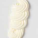 An overhead image of a squiggle of vegan cream cheese frosting, piped onto a flat white surface.