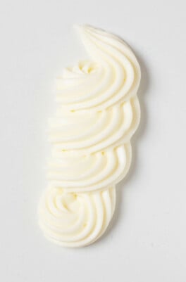 An overhead image of a squiggle of vegan cream cheese frosting, piped onto a flat white surface.