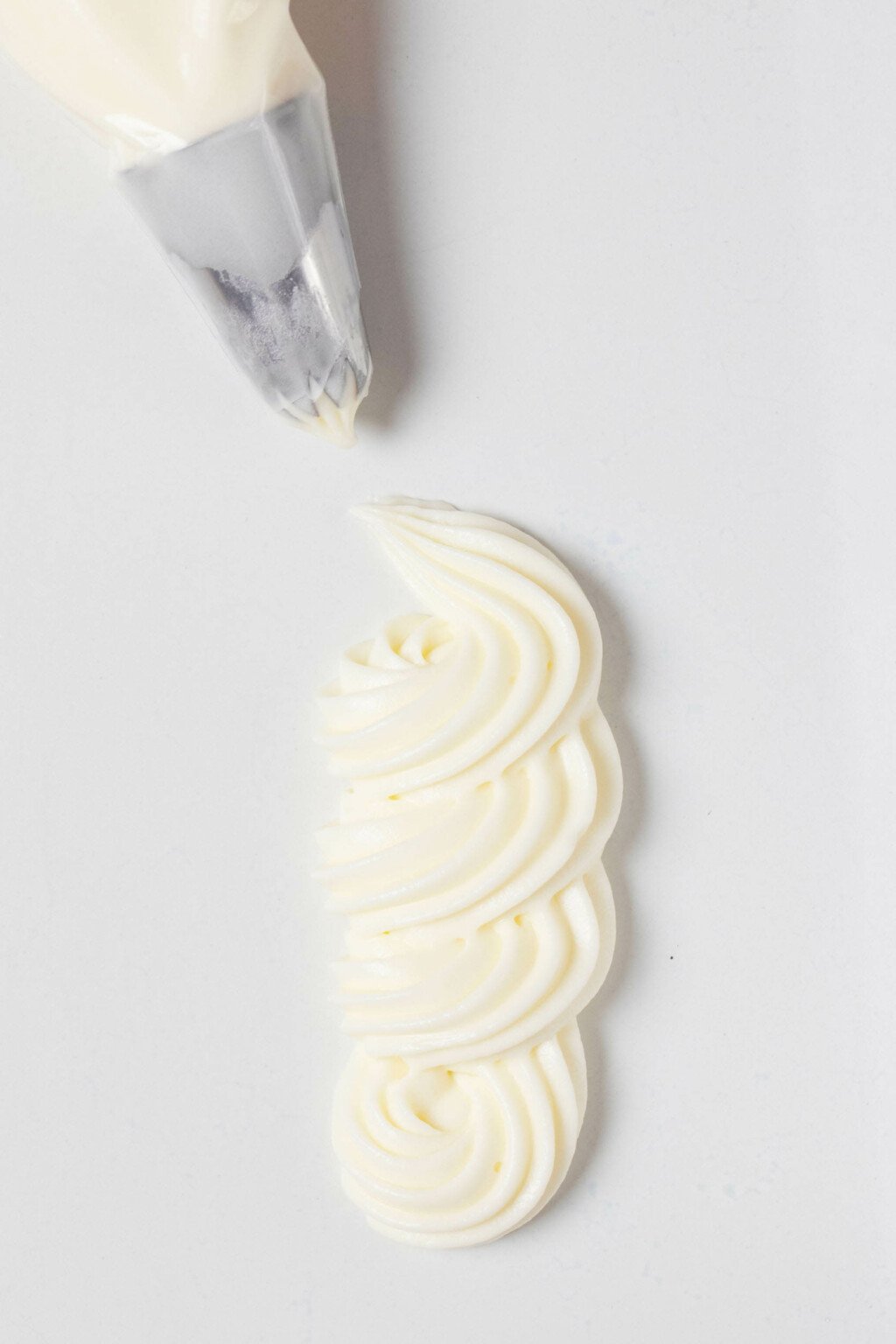 An overhead image of a squiggle of vegan cream cheese frosting, piped onto a flat white surface.