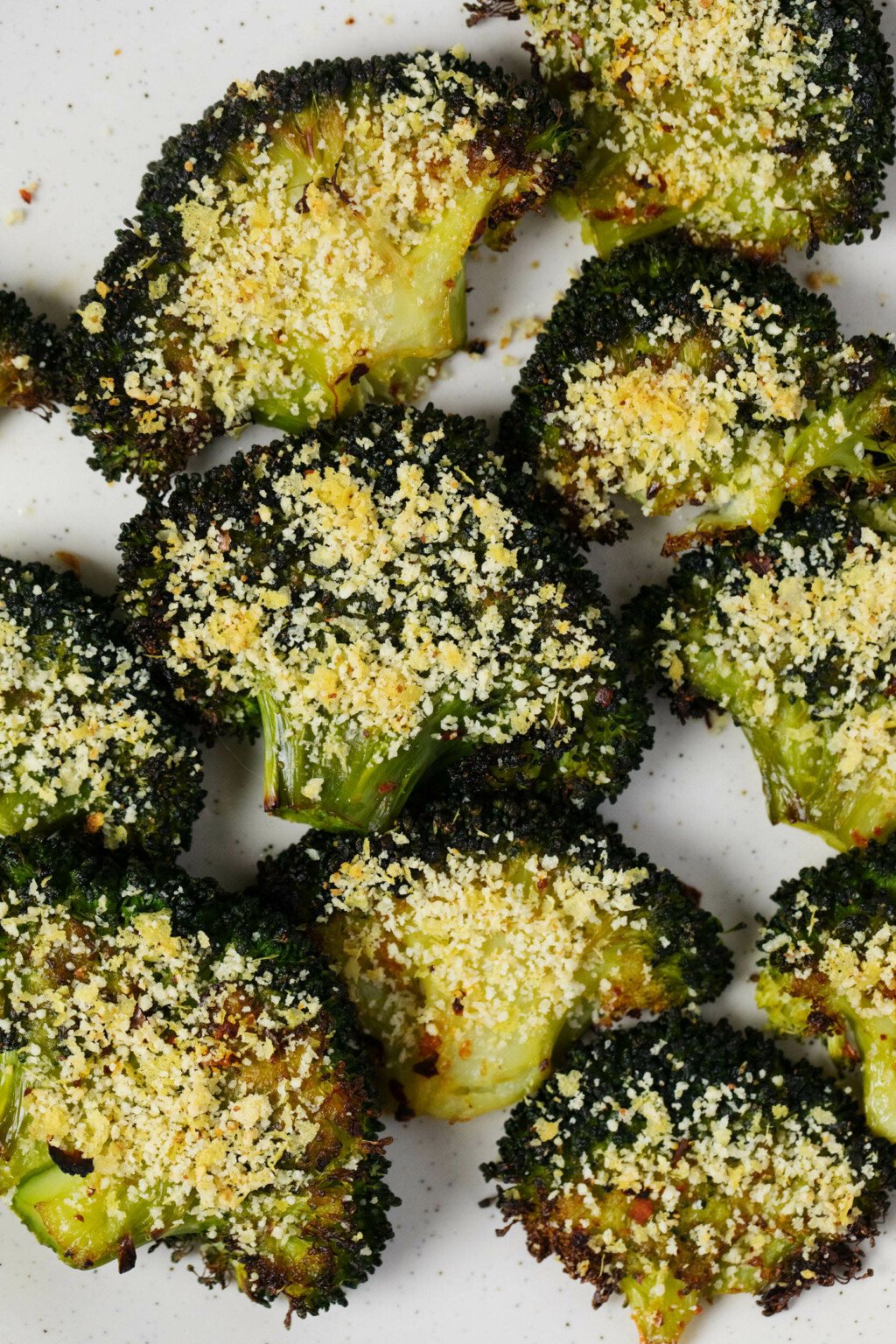 An overhead image of smashed broccoli florets that have been topped with a nut-based vegan 