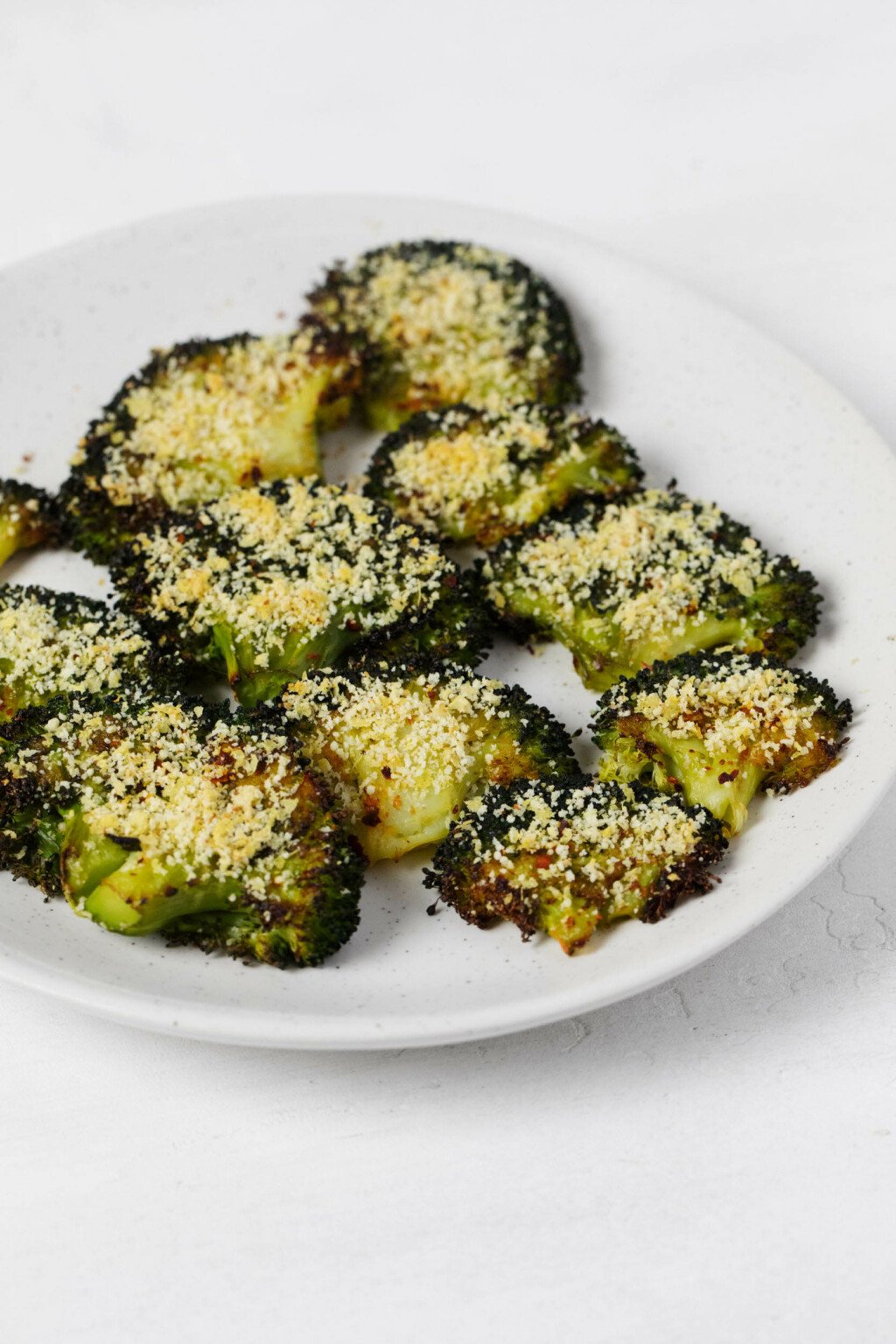 An overhead image of smashed broccoli florets that have been topped with a nut-based vegan "cheese" topping.