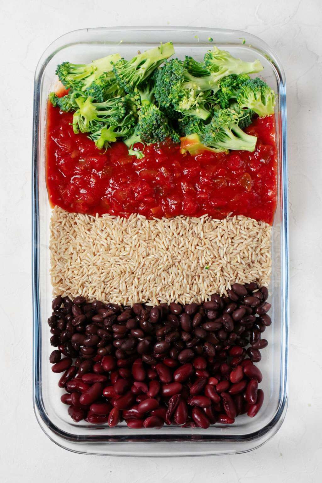 An overhead image of a casserole dish, which is filled with rice, beans, salsa, and broccoli.