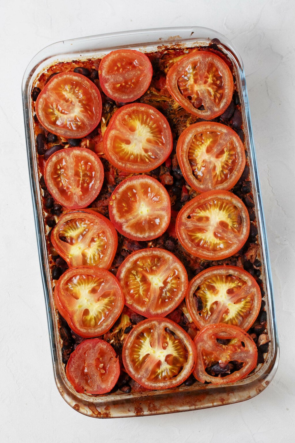 An overhead image of a baked rice dish that has been garnished with thin, round slices of tomato.