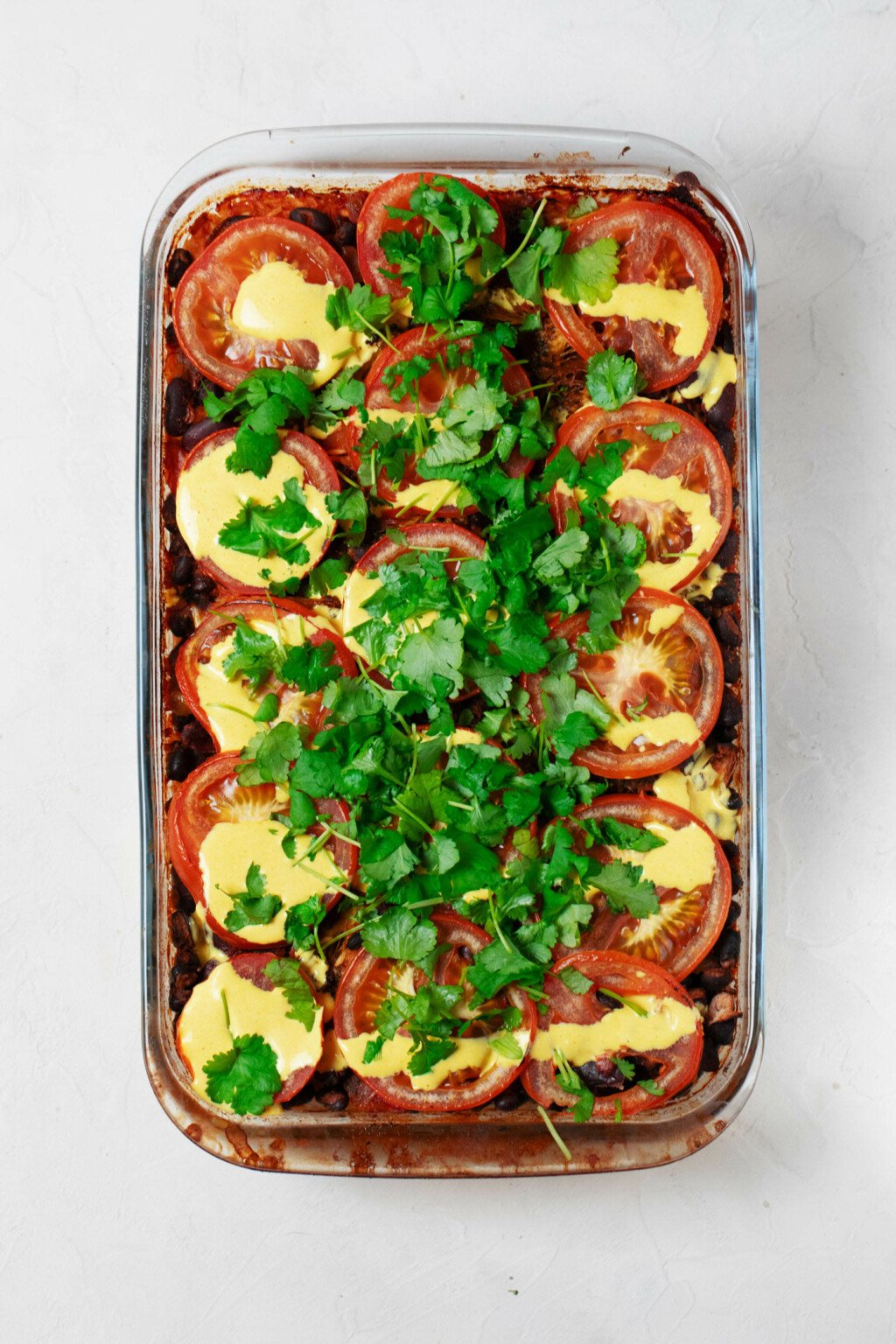 An overhead image of a vegan casserole dish that has been topped with herbs and a pale yellow sauce.