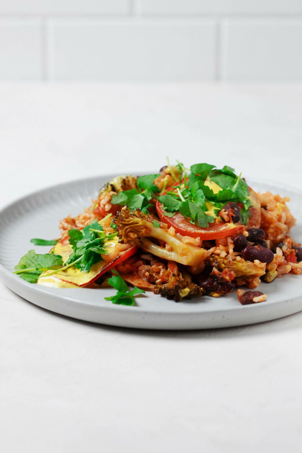 A photo of a round, grayish white plate, which has been topped by a bean and brown rice casserole. Green cilantro leaves are garnished on top.