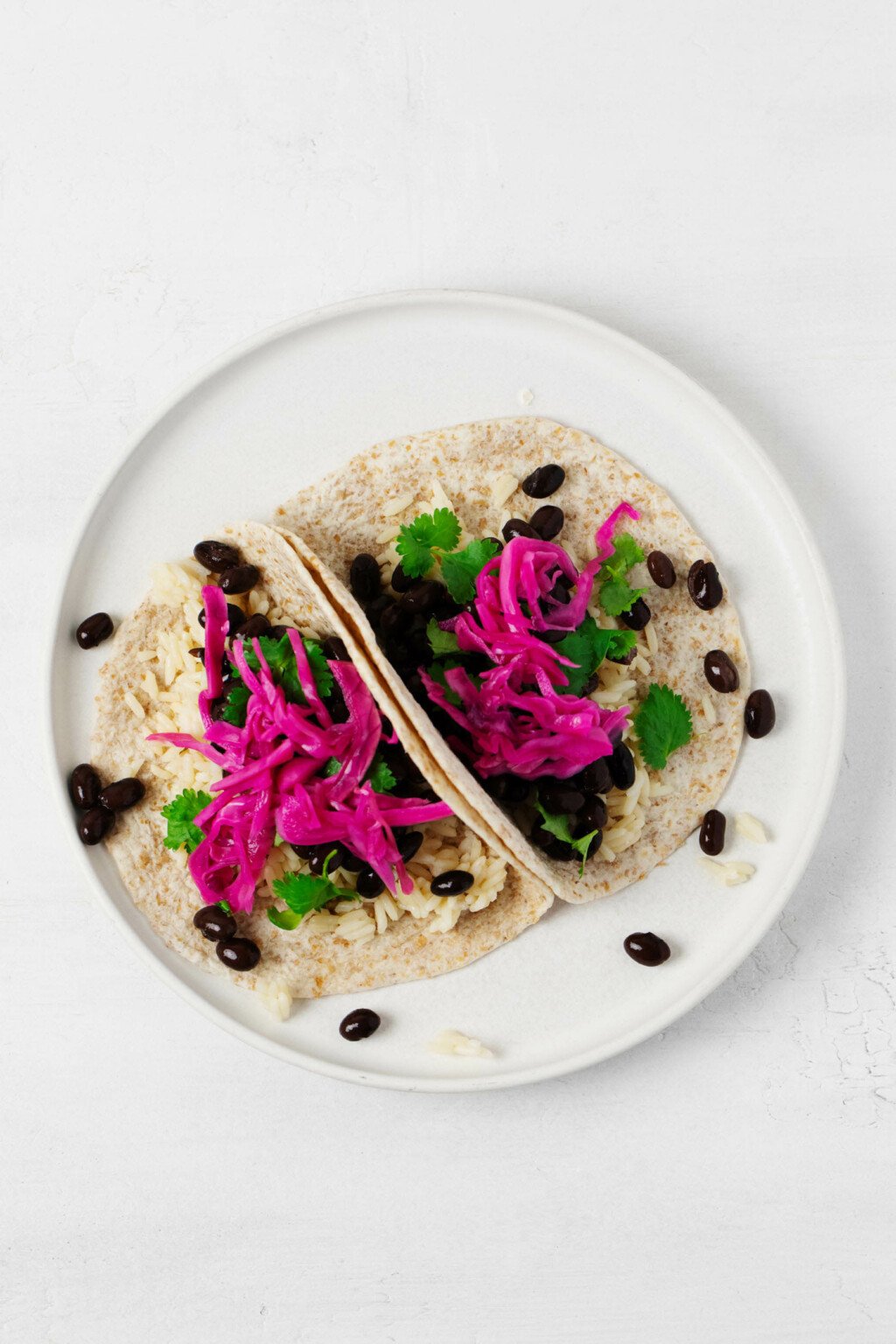 An overhead image of two rice and bean tacos, which have been garnished with quick pickled red cabbage.