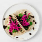 An overhead image of two rice and bean tacos, which have been garnished with quick pickled red cabbage.