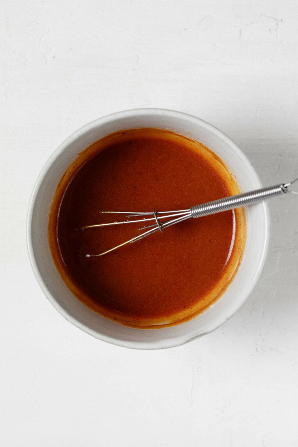 A red colored sauce is being whisked together in a small mixing bowl.