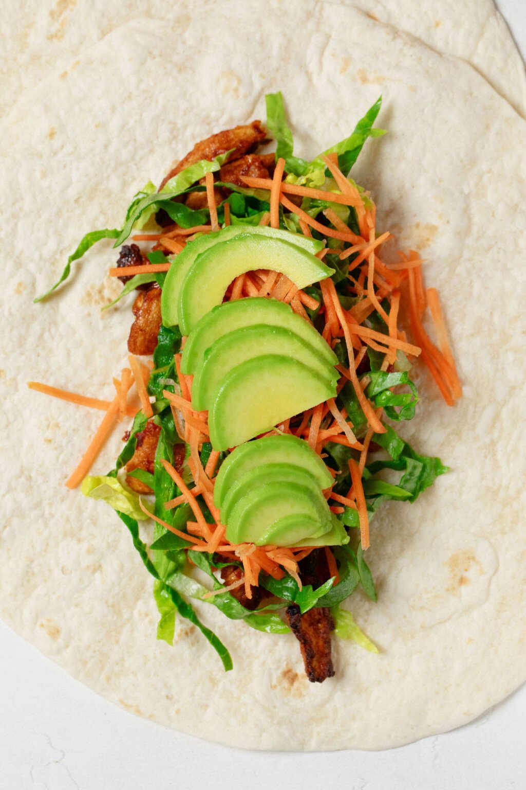 Avocado slices have been layered on top of other fillings for a plant-based “buffalo chicken” wrap.