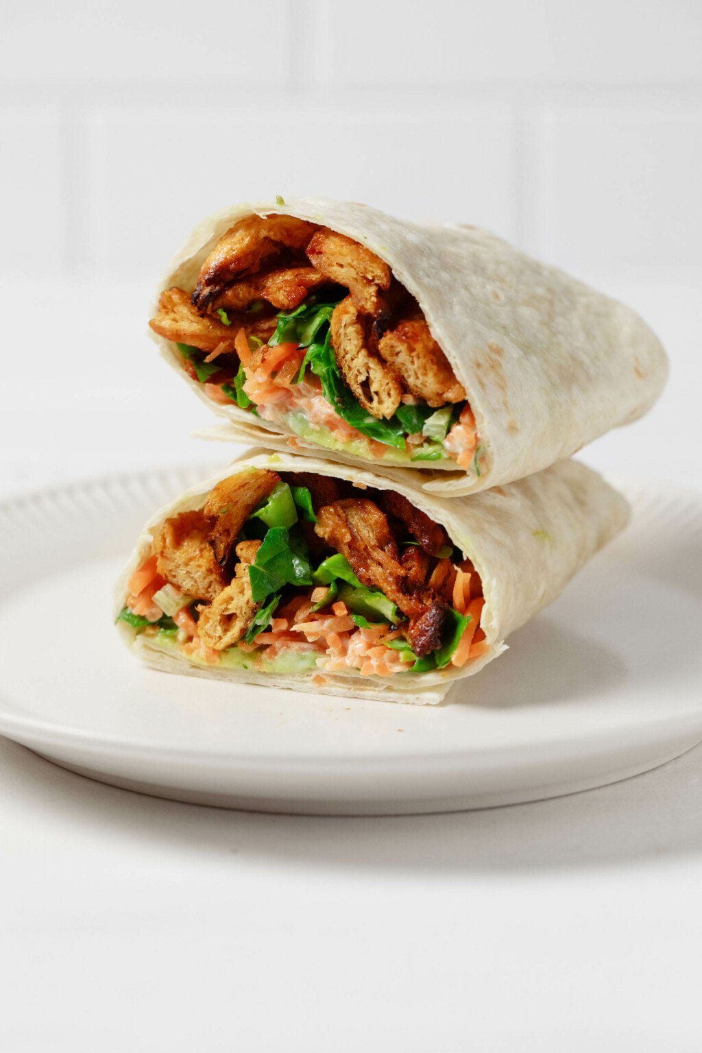 A vegan buffalo "chicken" wrap, made with plant-based soy curls, has been cut open. The two halves are stacked on top of one another.