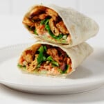 A vegan buffalo "chicken" wrap, made with plant-based soy curls, has been cut open. The two halves are stacked on top of one another.