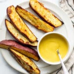 An overhead image of crispy roasted Japanese sweet potato wedges. They're arranged on a white platter with a bright yellow dipping sauce.