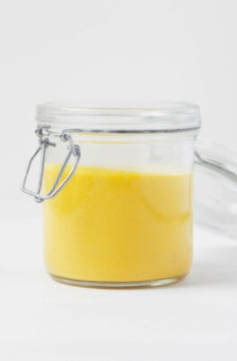 A sideways image of a mason jar, which has been filled with an electric gold, creamy sauce.