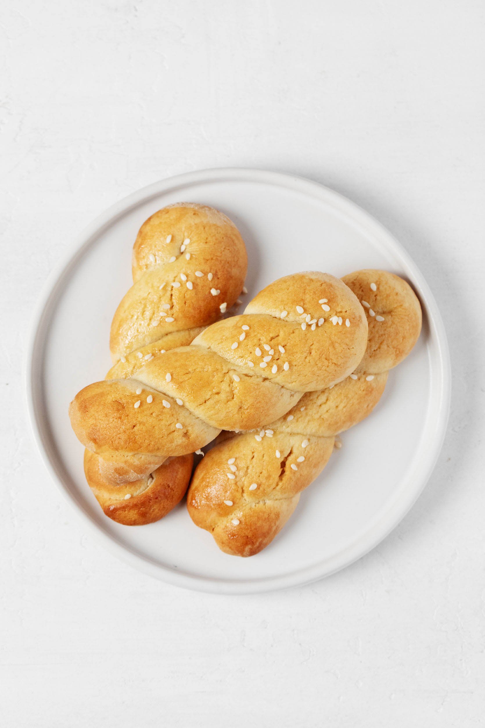 An overhead image of a small, round, rimmed white plate, which is topped with braided koulourakia cookies.