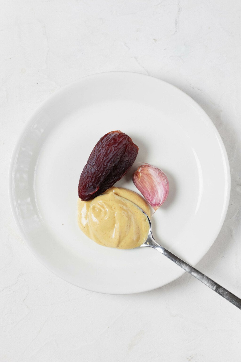 An overhead image of a small serving plate with a pitted date, mustard, and garlic.