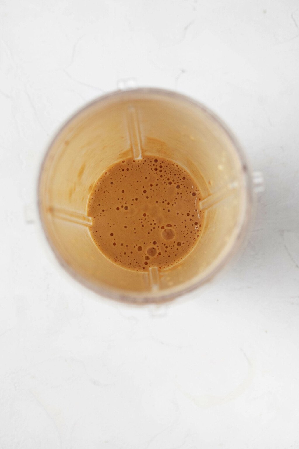 An overhead image of the container of a mini-blender filled with a creamy, cream colored dressing.