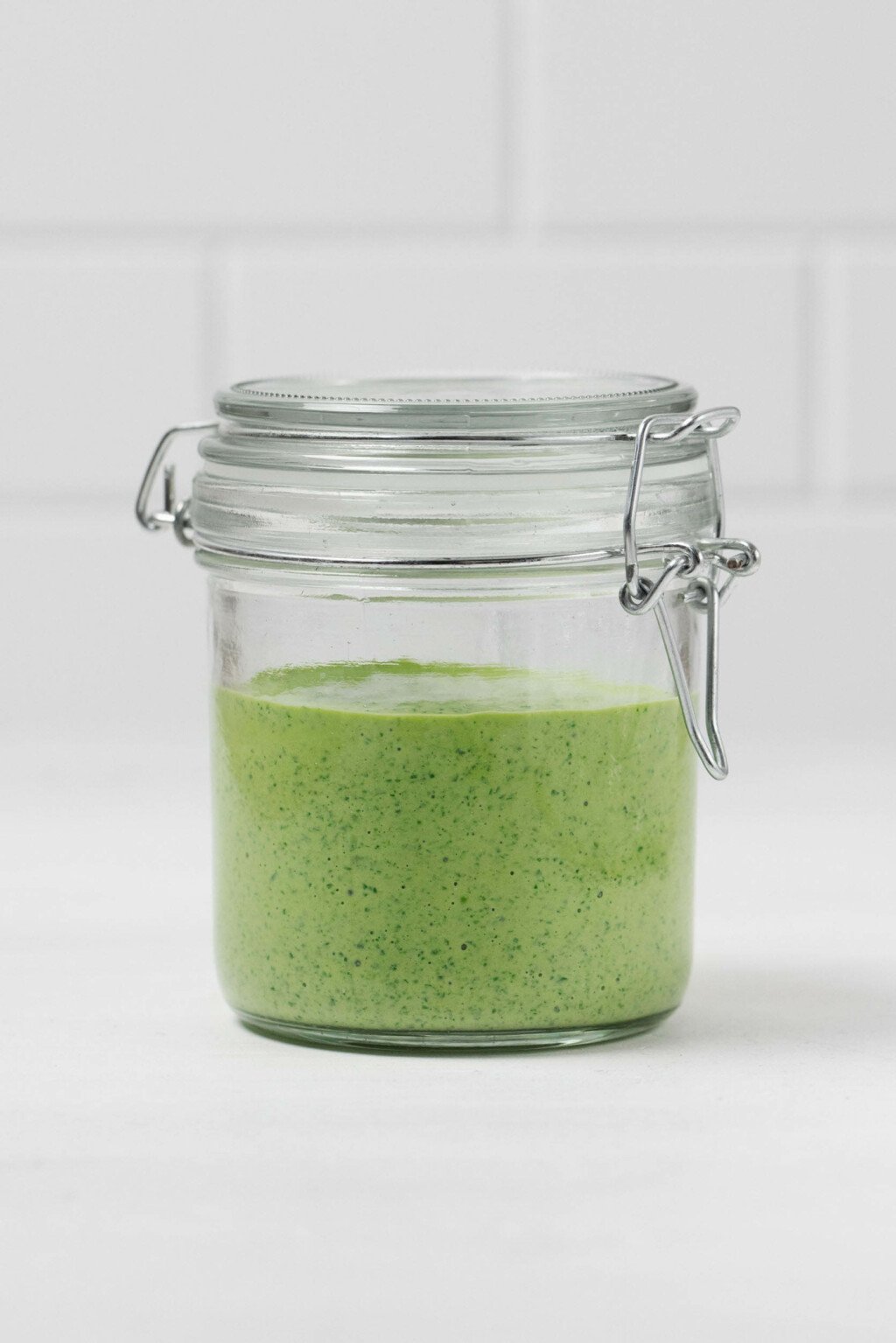 An image of a glass mason jar with a flip top lid, which holds a brighly colored green tahini dressing.