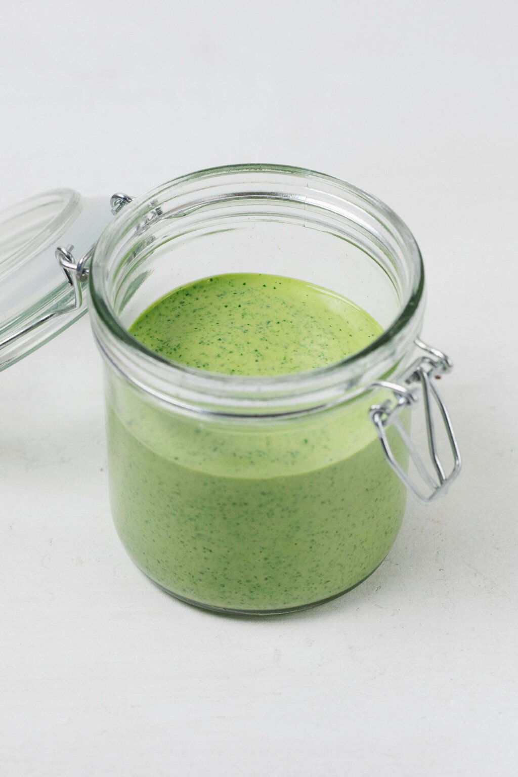 An image of a glass mason jar with a flip top lid, which holds a brightly colored green tahini dressing.