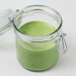 An image of a glass mason jar with a flip top lid, which holds a brighly colored green tahini dressing.