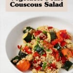 A roasted vegetable and pearl couscous salad has been arranged in a shallow, round white bowl. It rests on a white surface.