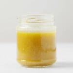 An angled image of a glass jar filled with red wine vinaigrette. It rests on a white surface.