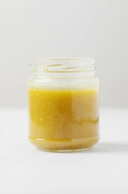 An angled image of a glass jar filled with red wine vinaigrette. It rests on a white surface.
