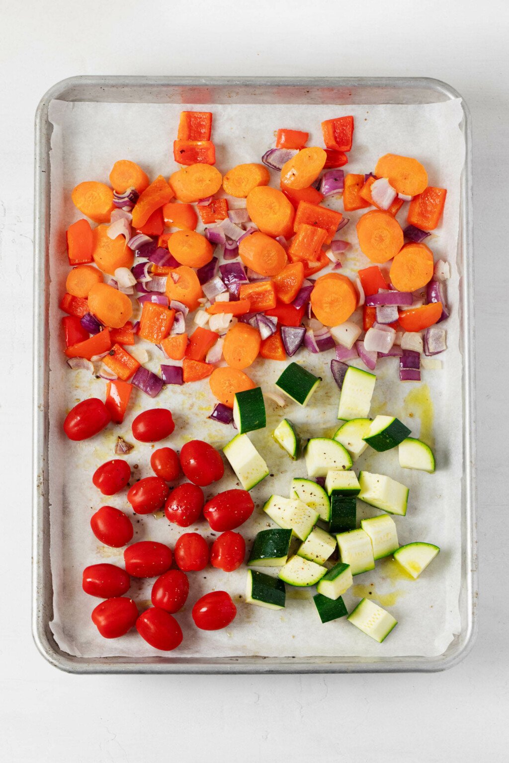 Colorful summer vegetables are arranged on a parchment-lined baking sheet, for roasting in the oven.