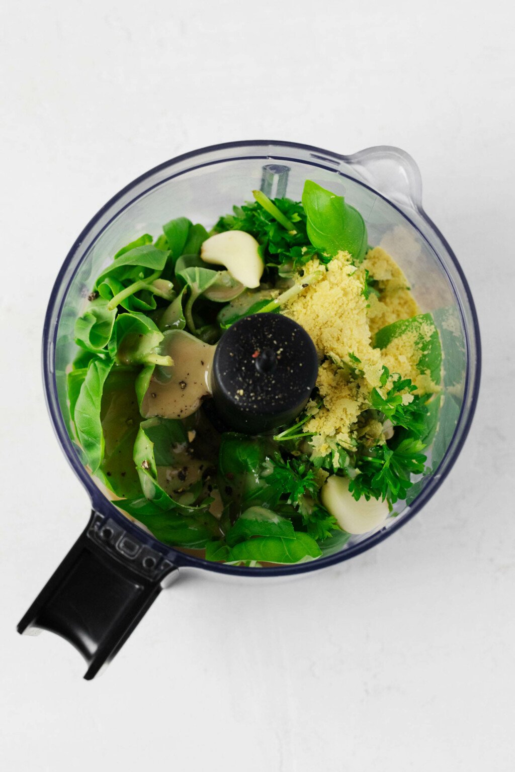 Nutritional yeast and fresh herbs have been placed into the bowl of a food processor.