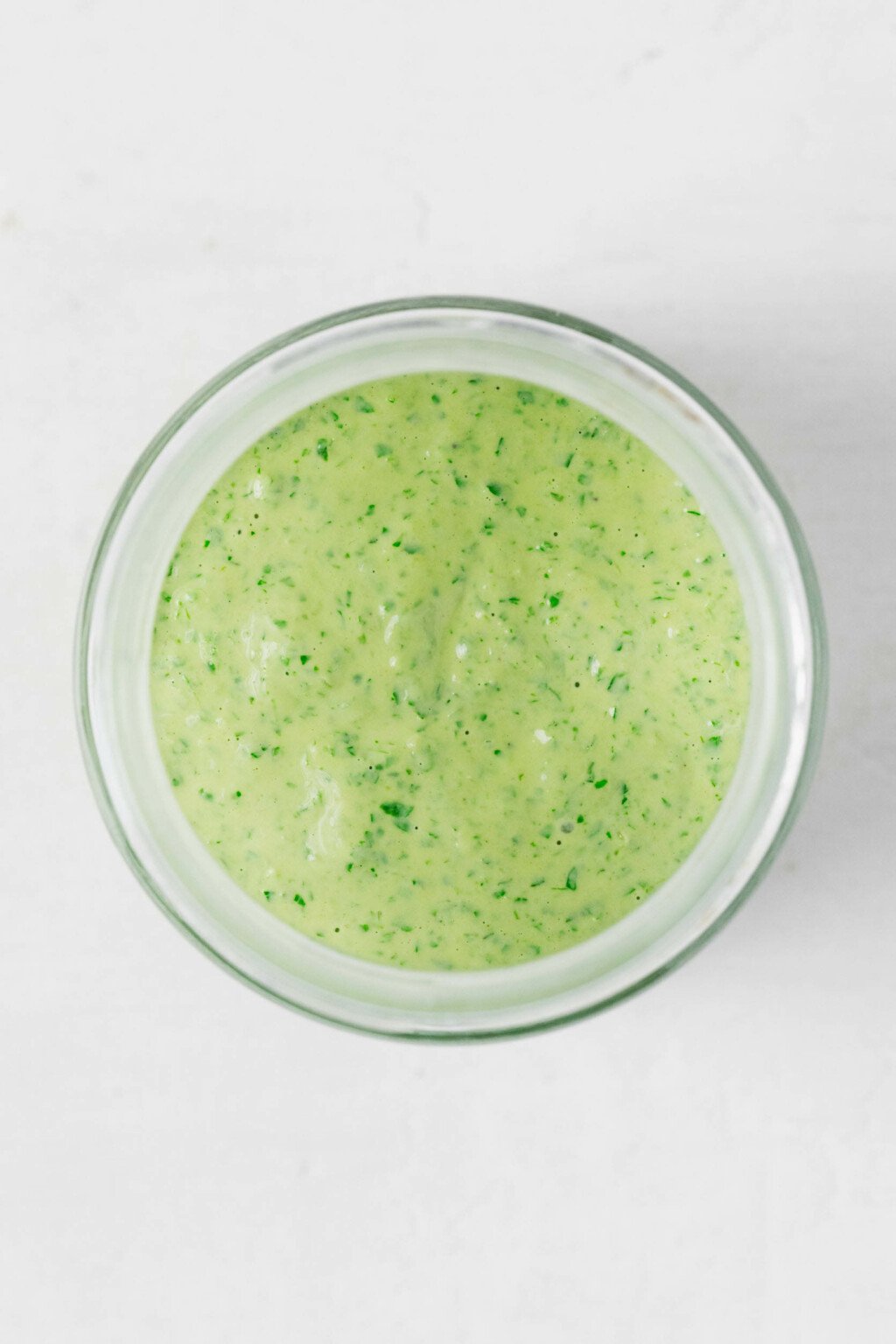 An overhead image of a glass jar, which has been filled with creamy tahini pesto.