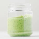 An image of a glass jar resting on a white surface. The jar has been filled with creamy tahini pesto.