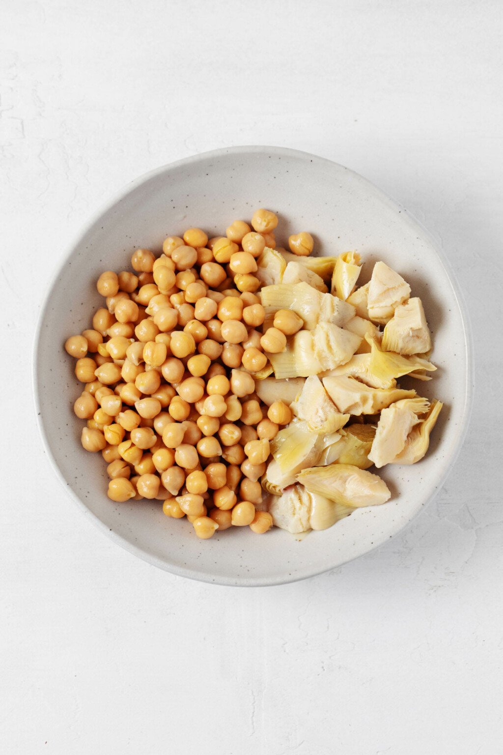 An overhead image of a white bowl containing cooked chickpeas and artichoke hearts.